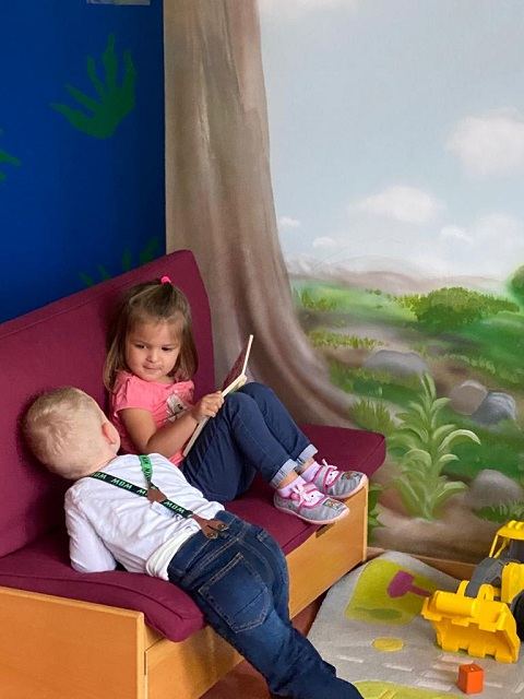 Ein Kind sitzt mit einem Buch auf dem Sofa in der Leseecke