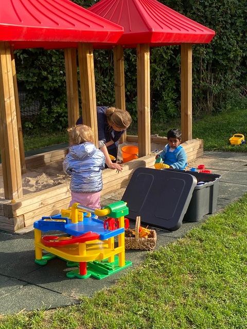 Sandkasten mit einem hölzernen Spielhaus daneben