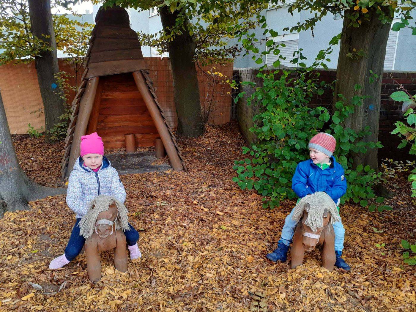 Zwei Holzpferde und ein Tipi stehen im Herbstlaub auf dem Außengelände